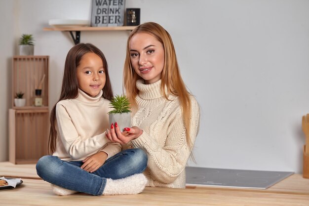 Beautiful mom and her small little daughter on weekend sitting on countertop consider a flower in a ...