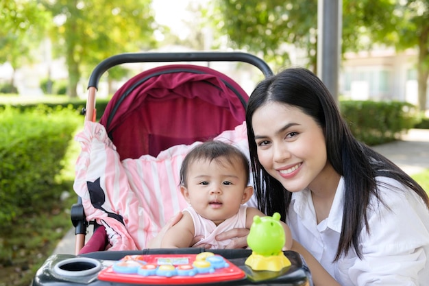 Beautiful mom with a baby girl sitting on baby trolley outdoor in sunshine day