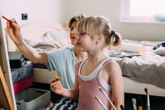 La bella madre artista e il suo bambino dipingono un quadro a casa con colori acrilici