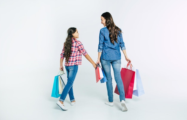 Beautiful mother and cute daughter in casual clothes with shopping bags in hands make purchases at the mall isolated on white