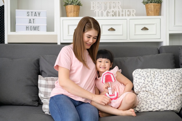 A beautiful mother and daughter are holding an artificial Dental Model Of Human Jaw in home, education and dental health concept.