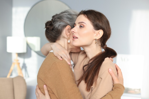 Bella madre e figlia. la giovane donna allegra sta abbracciando sua madre di mezza età nel soggiorno. ritratto di famiglia.
