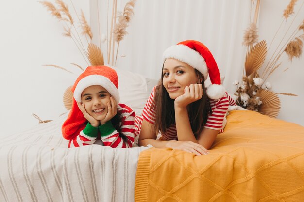 Beautiful mother and daughter in christmas pajamas hug and play at home in the bedroom on the bed. Christmas