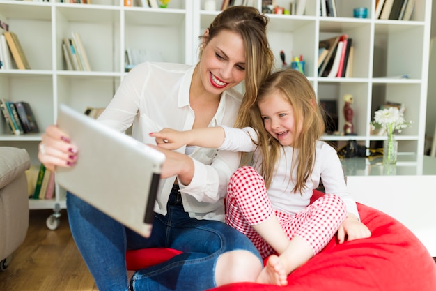 Beautiful mother and daughter playing with digital tablet at home.