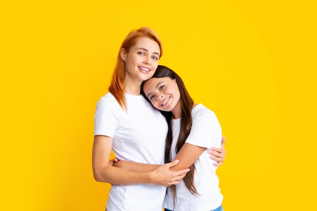 Beautiful mother and daughter smiling happy hugging over isolated yellow background