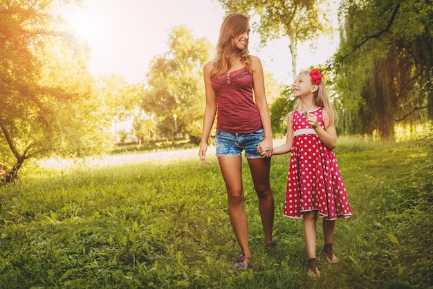 Beautiful mother and daughter walking through a park in spring day.