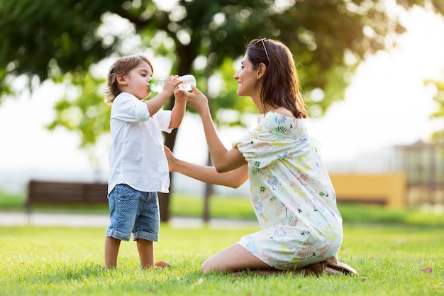 Beautiful mother gives child a drink of water in the park.