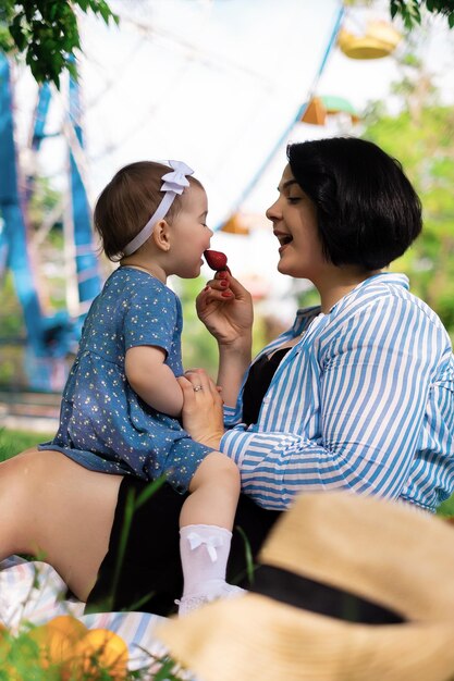 Beautiful mother and her cute daughter eat strawberries and tangerines in the park and enjoy a picnic day family weekend park vacation