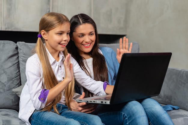 Beautiful mother and her daughter is having Skype call on laptop while sitting at home