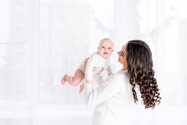 Bella madre che tiene un bambino in braccio alla finestra di casa, il concetto di una famiglia felice e amorevole, stile di vita