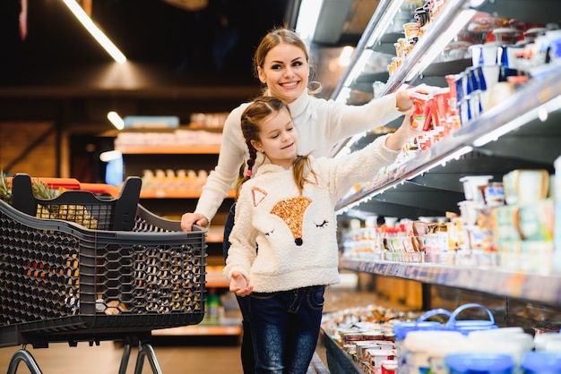 Beautiful mother holding grocery basket with her child walking in supermarket 