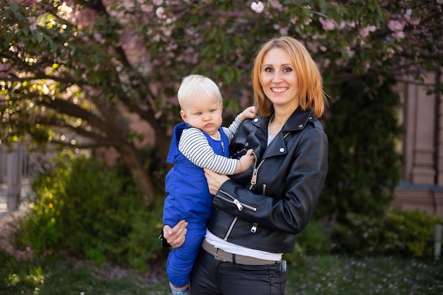 La bella madre tiene tra le braccia un piccolo figlio carino mamma e bambino in un giardino fiorito sakura