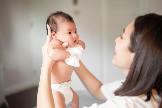 美しい母親は寝室で彼女の生まれたばかりの赤ちゃんと遊んでいます。