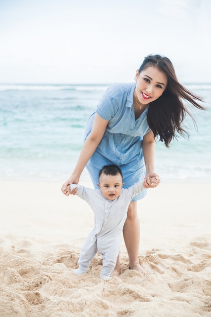 Beautiful mother is teaching her son walks on the beach