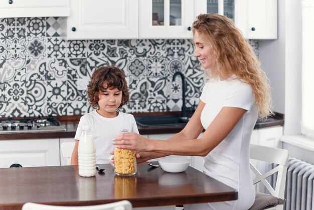 beautiful mother prepares healthy breakfast from cornflakes and milk for her beloved son