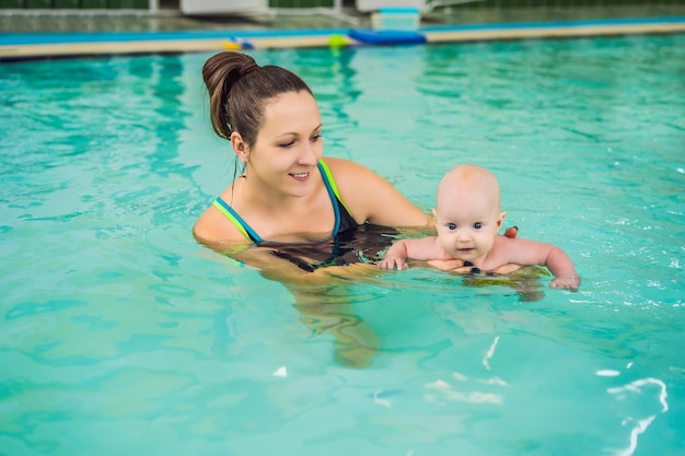 Beautiful mother teaching cute baby girl how to swim in a swimming pool Child having fun in water with mom