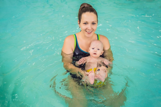 Beautiful mother teaching cute baby girl how to swim in a swimming pool Child having fun in water with mom