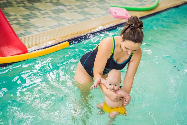 Beautiful mother teaching cute baby girl how to swim in a swimming pool Child having fun in water with mom