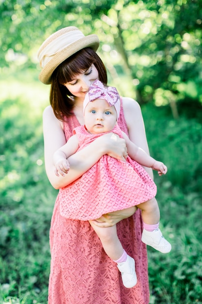 Beautiful Mother with the straw hat And her little daughter outdoors family look in in a pink dress . Outdoor Portrait of happy family. family look. Positive human emotions, feelings, emotions.