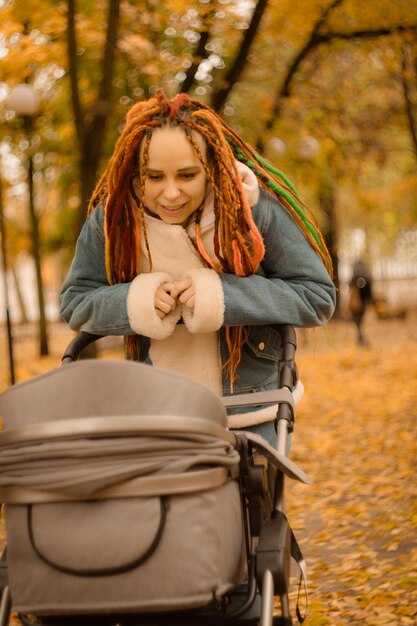 Photo beautiful mother with stroller in autumn park motherhood concept