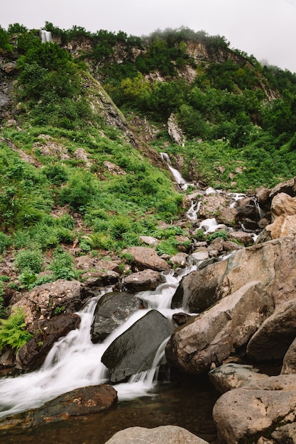 Bella cascata di montagna tra gli alberi estate sfondo naturale foto verticale