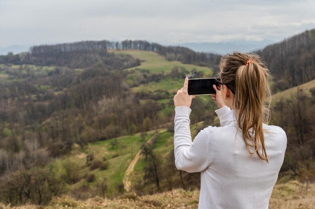 Beautiful mountains and standing young woman takes a photo top hills Landscape with mountain peak forest Travel concept