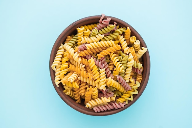 Beautiful multicolored pasta in bowl on blue background