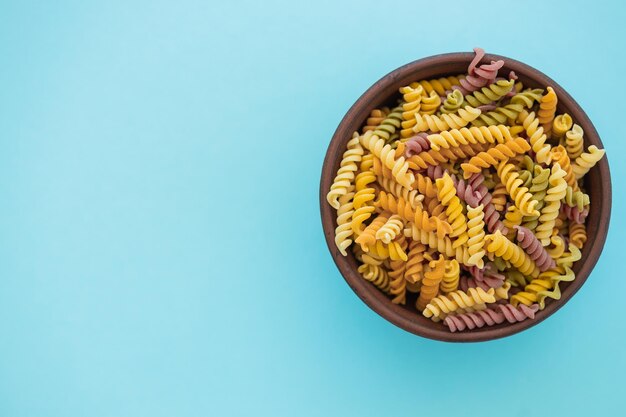 Beautiful multicolored pasta in bowl on blue background