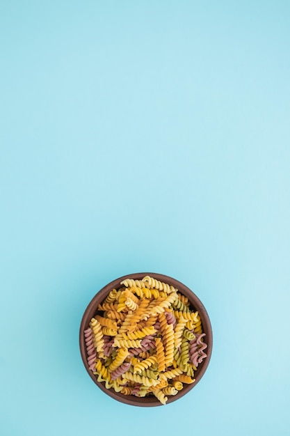 Beautiful multicolored pasta in bowl on blue background