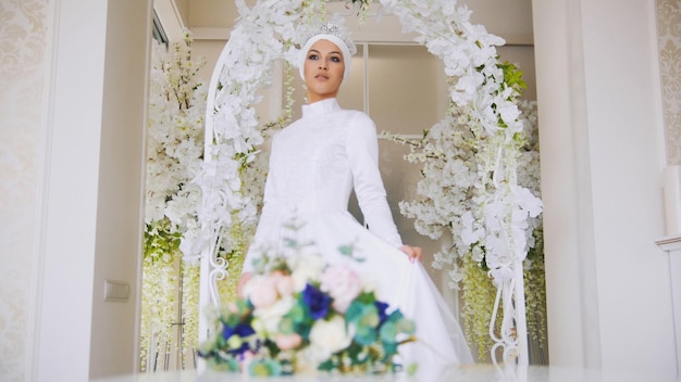 Beautiful muslim bride with make up in white wedding dress comes to the flowers