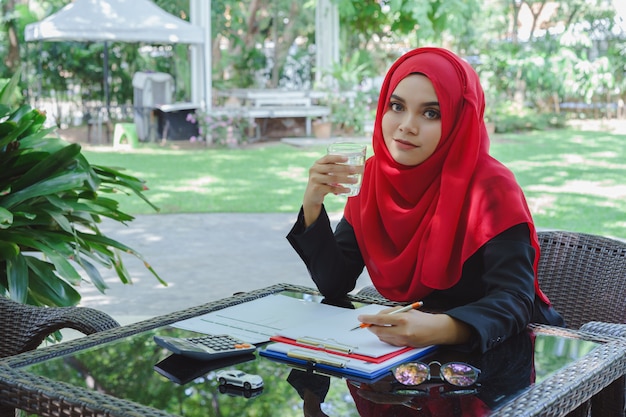 Beautiful Muslim business woman red hijab working outdoors and drinking water