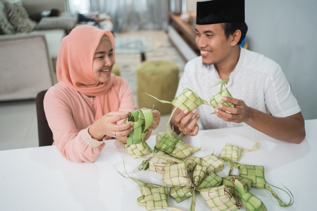 Beautiful muslim couple asian making ketupat rice cake at home using palm leaf