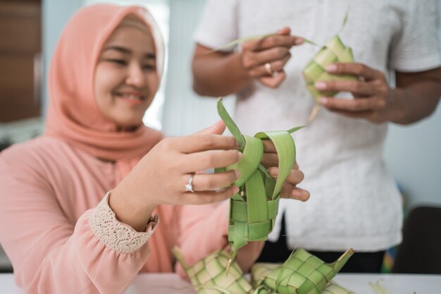 Beautiful muslim couple asian making ketupat rice cake at home using palm leaf