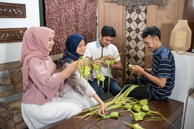 Beautiful muslim family and friend making ketupat rice cake at home using palm leaf for eid fitr mubarak tradition