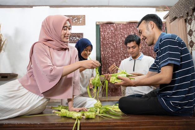 Bella famiglia musulmana e amico che fanno la torta di riso ketupat a casa usando foglie di palma per la tradizione eid fitr mubarak