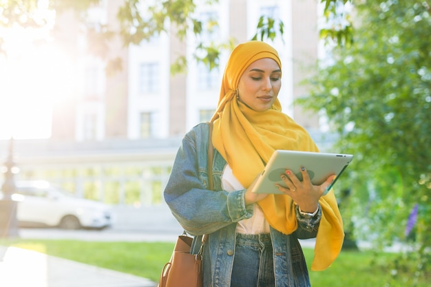 밝은 노란색 hijab 지주 태블릿을 입고 아름 다운 이슬람 여성 학생