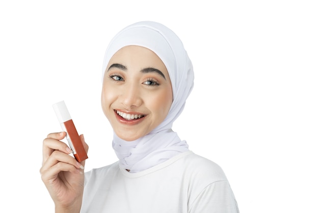 Beautiful muslim girl in hijab looking at camera while holding lipstick bottle