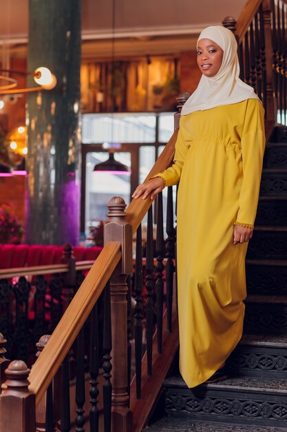 Beautiful Muslim girl in hijab smiling, waiting for her food in a restaurant.