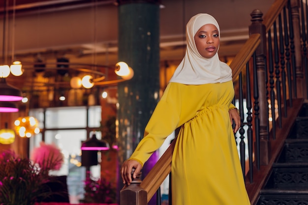 Bella ragazza musulmana in hijab sorridente, aspettando il suo cibo in un ristorante.