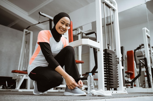 Beautiful muslim girl tying shoelaces on sports shoes in gym