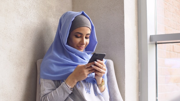 Photo beautiful muslim girl using smartphone in cafe. modern muslim woman and new technologies.