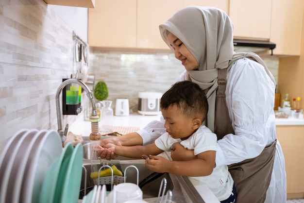 美しいイスラム教徒の母親が台所の流し台で息子の手を洗う