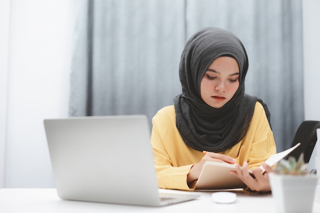 自宅でオンラインで学習するラップトップコンピューターを使用して美しいイスラム教徒の学生の女の子。オンライン教育の遠隔学習。