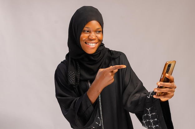 Beautiful muslin lady smiling as she points to her phone