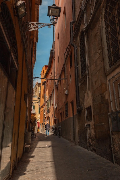 Beautiful narrow street with vintage houses buildings and an\
old man walking in italy traveling in europe with ancient\
architecture in sunlight and shadow