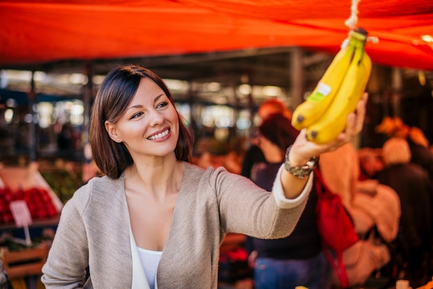 Beautiful natural brunette buying bananas at green market.
