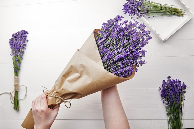 Beautiful natural lavender flowers bouquet wrapped in paper in woman hands over white wooden