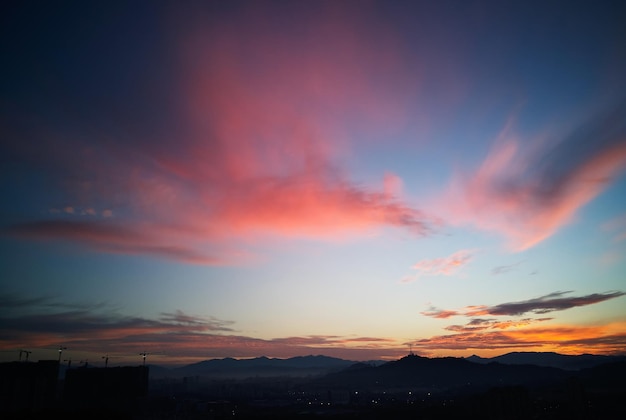 シルエットの街のスカイラインとその上の素晴らしいオレンジ色の雲の青い空に美しい自然の夕日の日の出