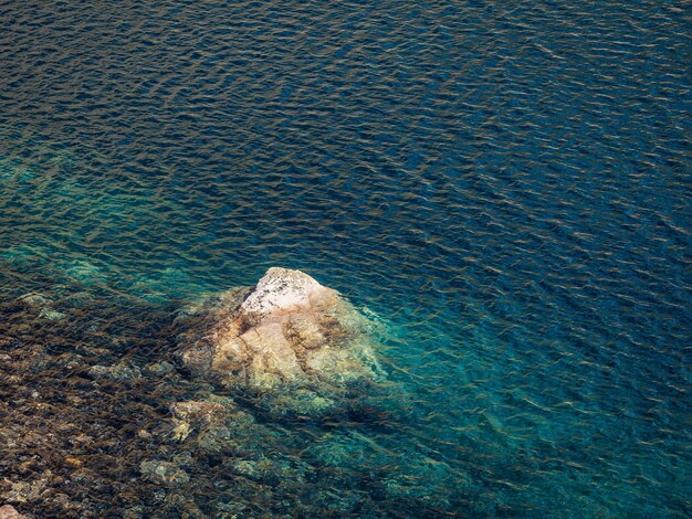 Красивый фон природы каменистого дна в бирюзовой прозрачной воде ледникового озера в солнечном свете. Солнечный фон с множеством камней в зеленой чистой воде ледникового озера.