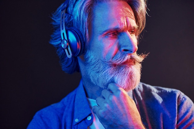 Beautiful neon lighting Stylish modern senior man with gray hair and beard is indoors